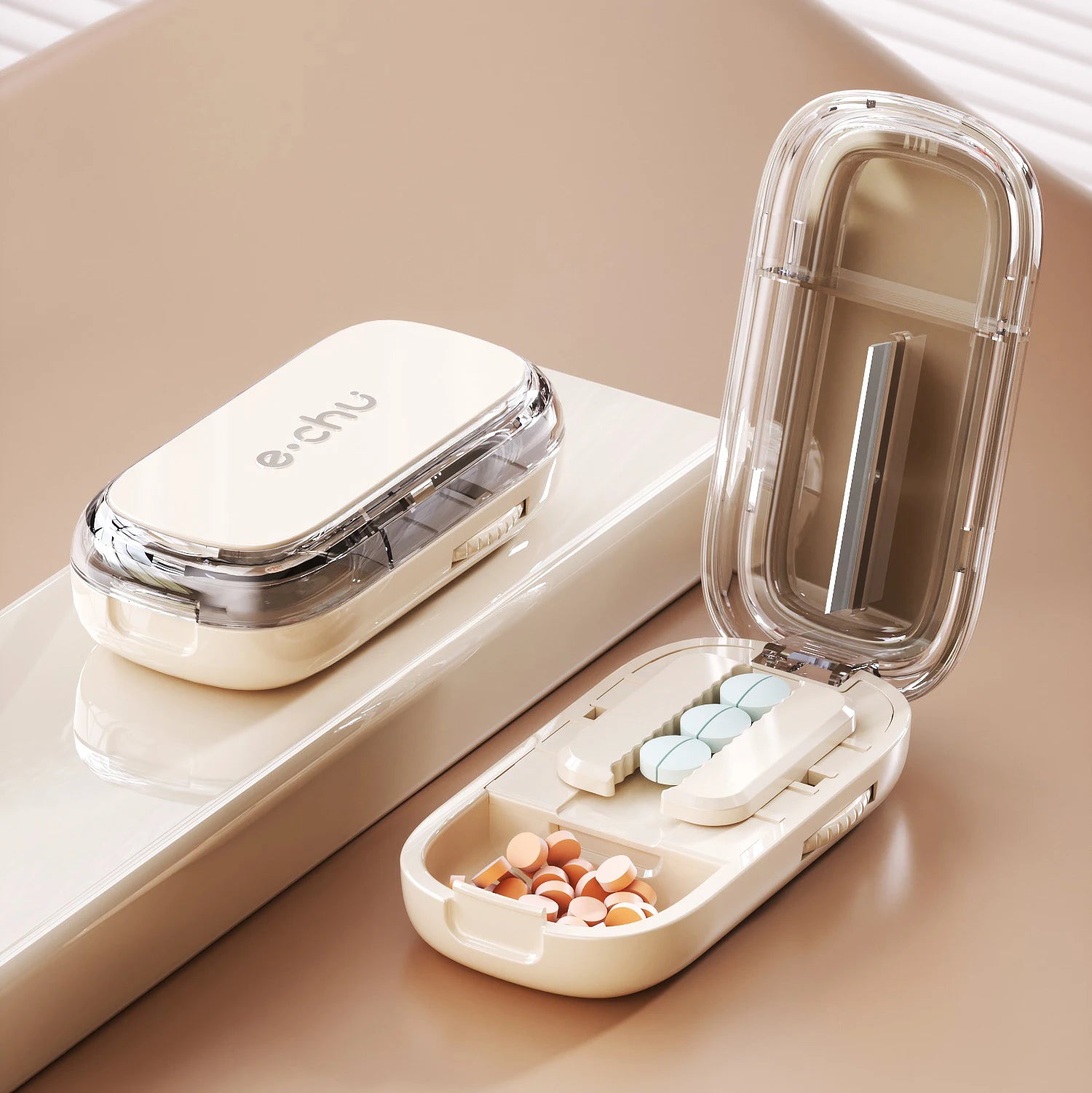 Beige Adjustable Pill Cutter by e.chu, open with pills in compartments, shown with a closed unit on a beige surface with blinds in the background.