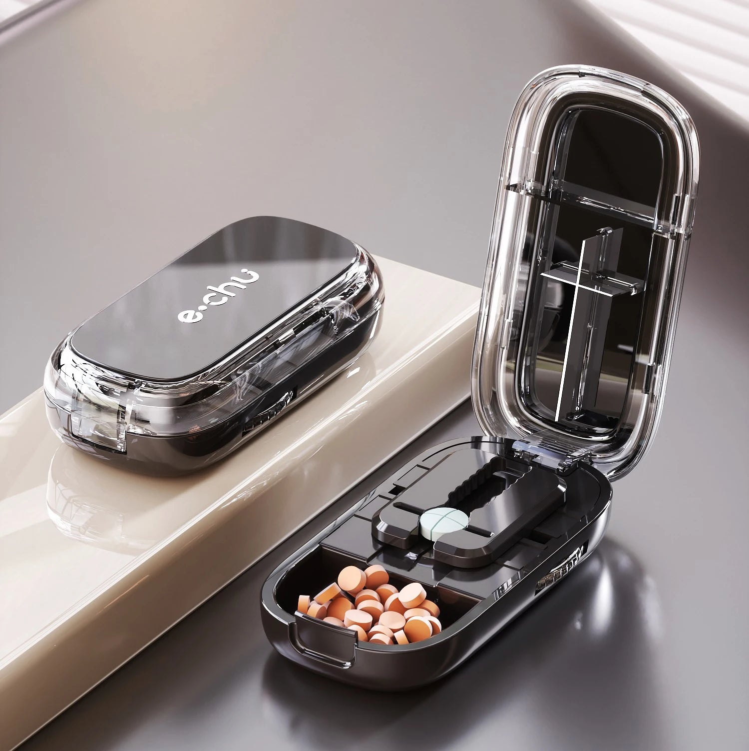 Black Adjustable Pill Cutter by e.chu, open with a top-down view showing pills in compartments and a pill in the cutting slot.