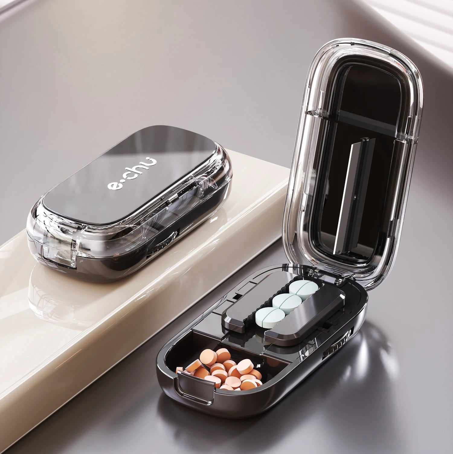 Black Adjustable Pill Cutter by e.chu, open with pills in storage compartments and a pill in the cutting slot, on a beige surface.