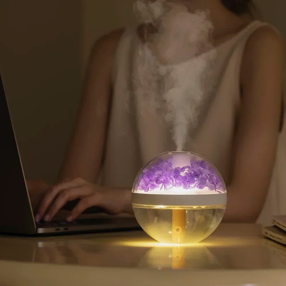 Person using a laptop with a glowing spherical diffuser emitting mist on a table.