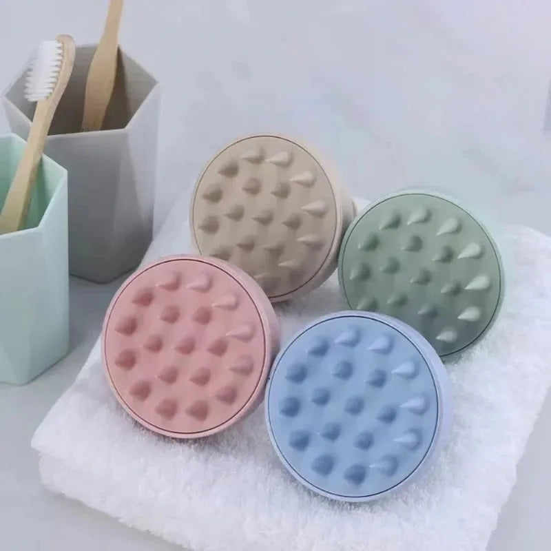 Four Silicone Shampoo Brushes in pink, beige, green, and blue, placed on a white towel with a toothbrush holder in the background.