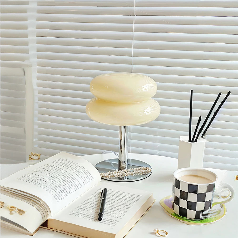 Table with an open book, coffee cup, and decorative items against a window with blinds.