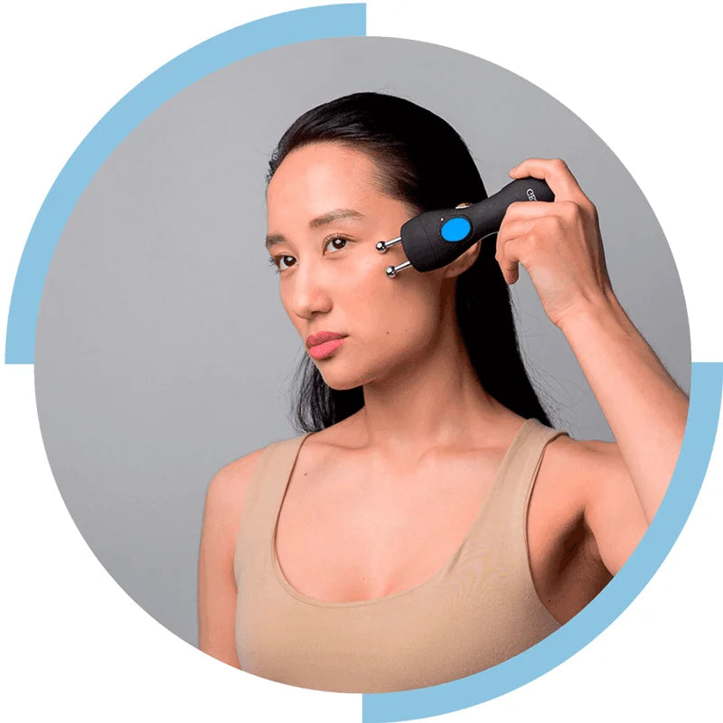 Woman using a handheld device on her face against a gray background