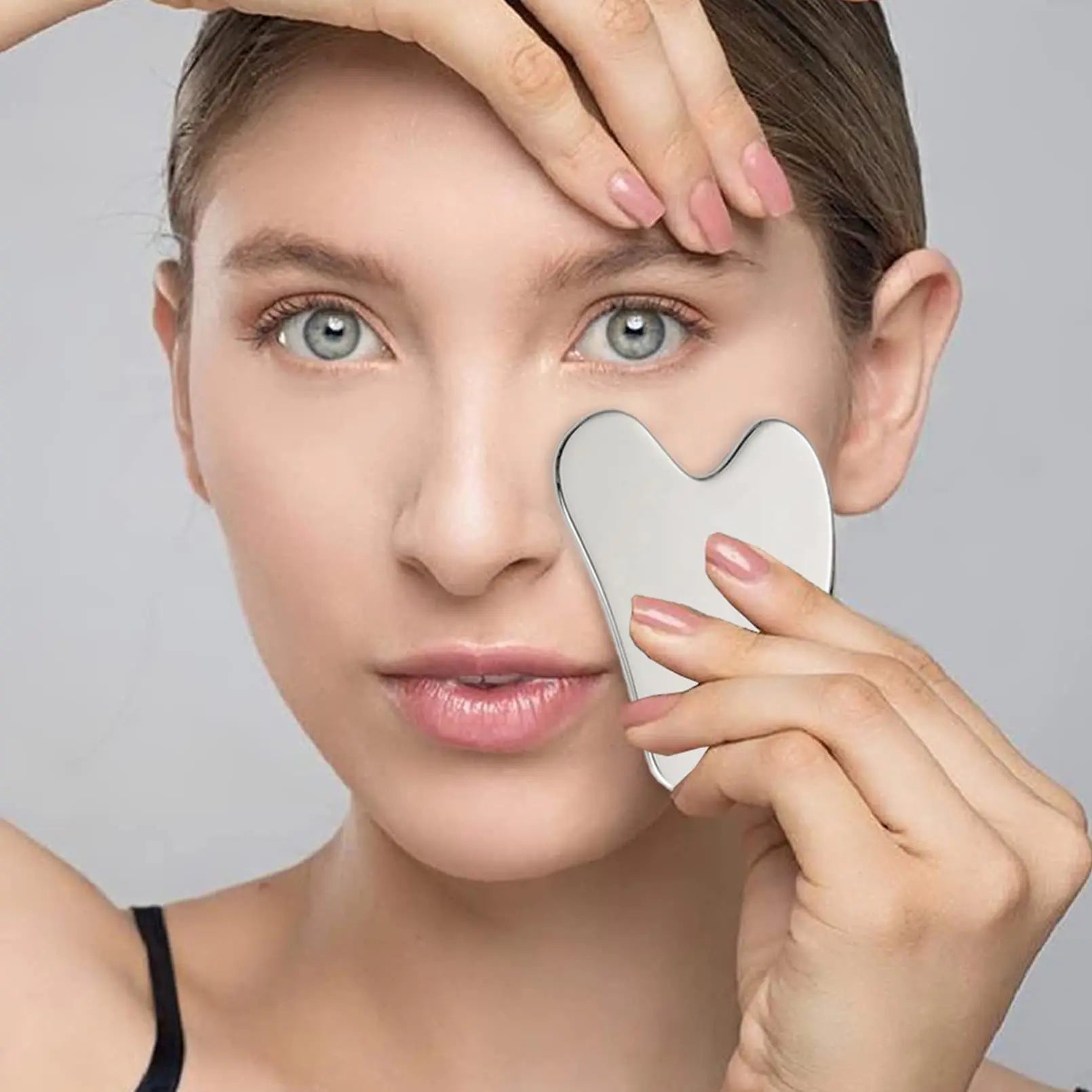 Woman using a skincare tool on her face against a neutral background